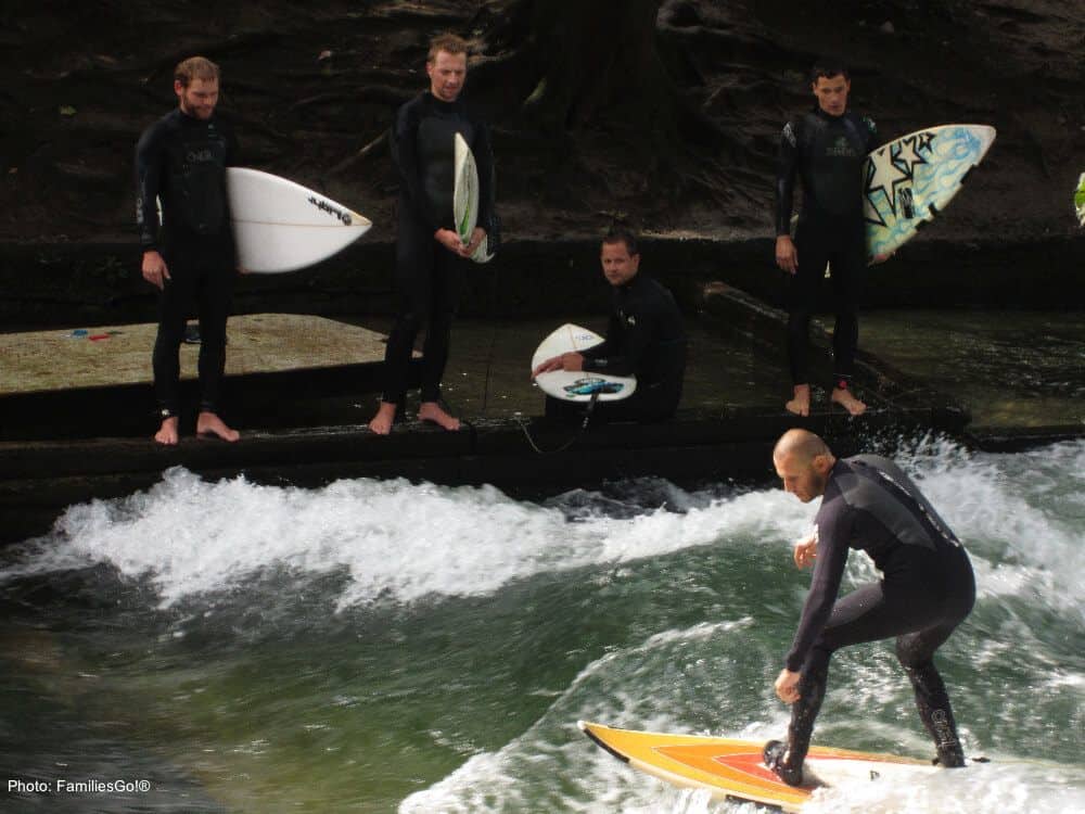 Eisbach surfers in wetsuits try to stay standing in englisher garten in munich.