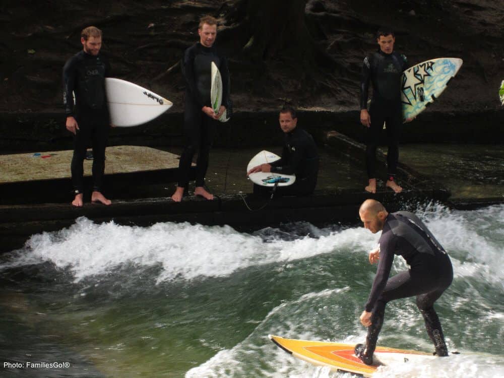 eisbach surfers in wetsuits try to stay standing in englisher garten in munich.