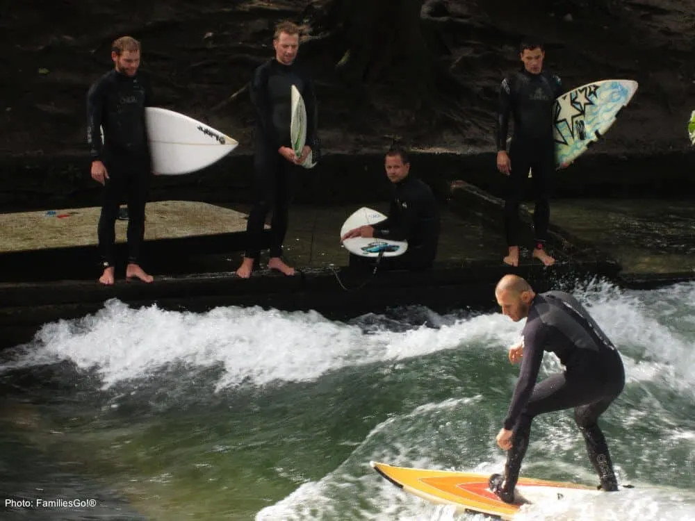 eisbach surfers in wetsuits try to stay standing in englisher garten in munich.