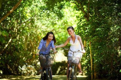 Biking can be the basis for a great family vacation with teens. Here a mom and daughter ride down a woodsy path together.