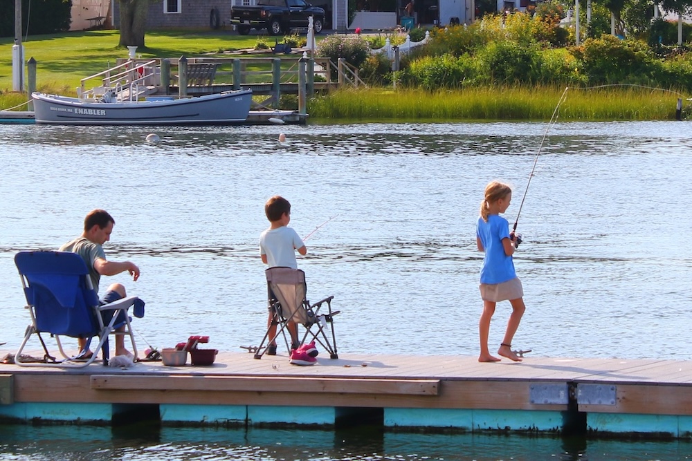 A dad and two kids fish off of a dock on cape cod, one of many cheap and easy things for families to do here.