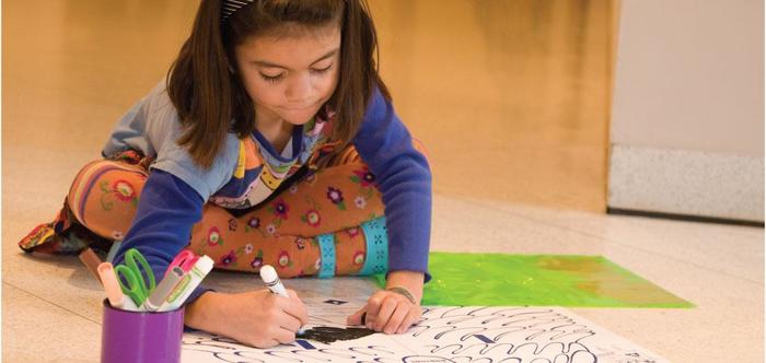 A girl colors on the floor of the denver art museum