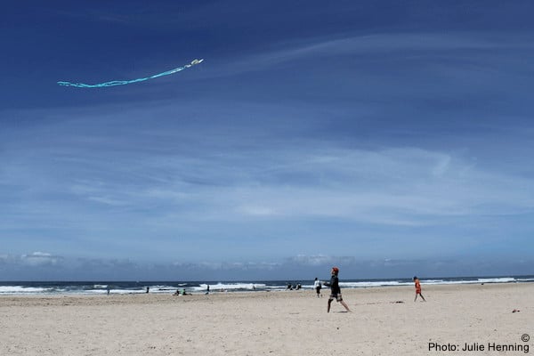 A family flies a kite on rockaway beach in oregon. The beach is empty, the sky is blue.