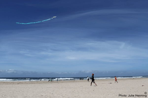 a family flies a kite on rockaway beach in oregon. the beach is empty, the sky is blue.