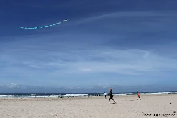 a family flies a kite on rockaway beach in oregon. the beach is empty, the sky is blue.