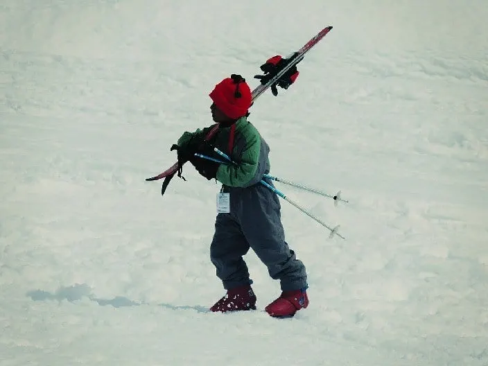 ski trips with kids build self-reliance. here a younng boy carries his skis annd polls back to the lodge.