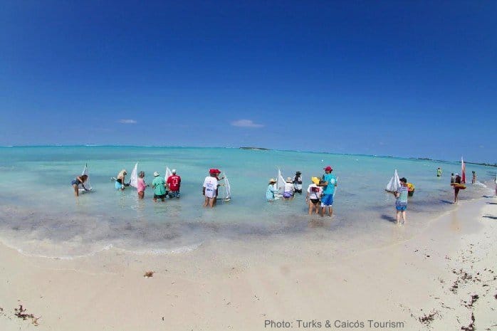 Kids and adults sailing toy boats on a beach in the turks & caicos