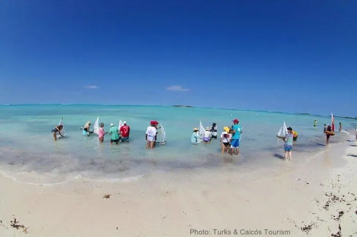 kids and adults sailing toy boats on a beach in the turks & caicos