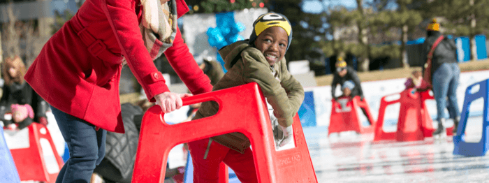 Ice skating in the park in downtown denver. Two kids use skating helpers.