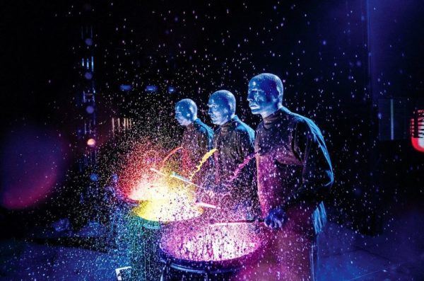 blue man group has fun with paint, here they've poured it on lit up drums before banging away. 