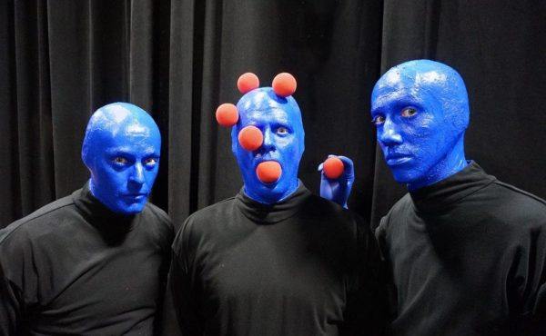 blue man group eats weird stuff. here they're eating red ping pong balls stuck to their heads. 