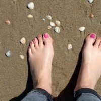 feet on a beach with pink toenails