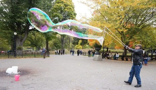 a man makes giant bubbles in new york city's central park.