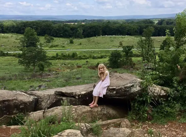 a child sits on a rock at little roundtop, bored.