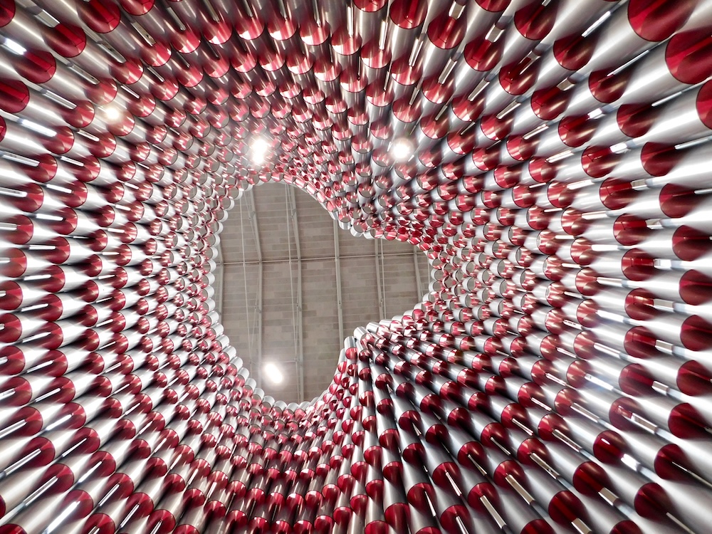 A view from inside a towering cone made of large metal and plastic pins in the atrium of the building museum