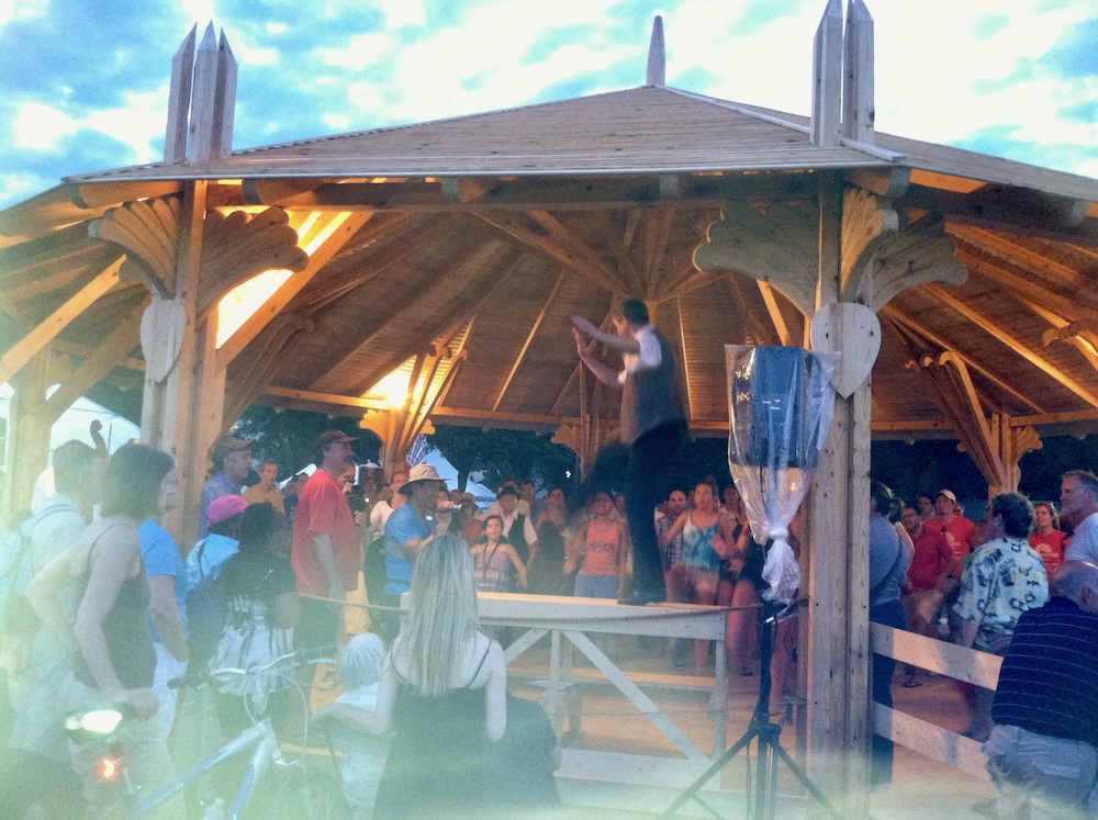 A man stands on a table to demonstrate hungarian dancing to a crowd at the smithsonian folklife festival.
