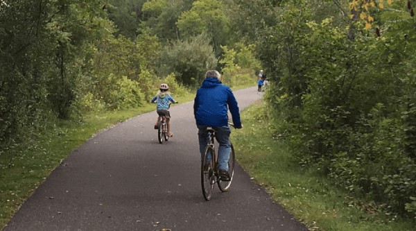 A dad and daughter ride bikes on the wide, flat and green  ashuwillticook rail trail.