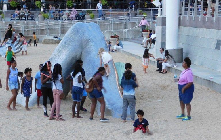 A girl climbs the leg of a stone giant as other kids watch.