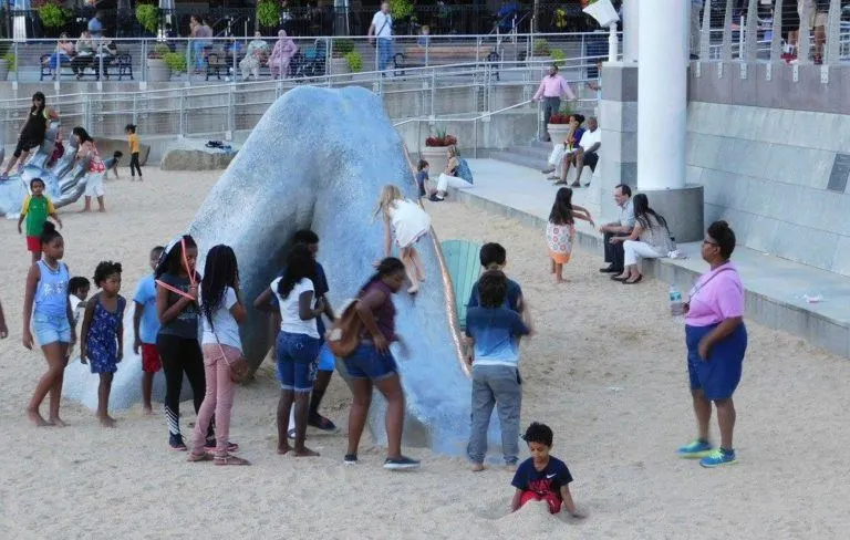 a girl climbs the leg of a stone giant as other kids watch. 