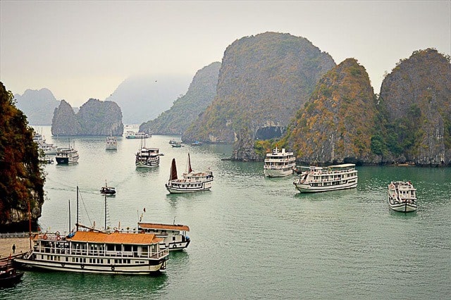 Halong bay provides a scenic break from vietnam's busy cities. Here, small tourist cruise boats dot the bay with caves behind.