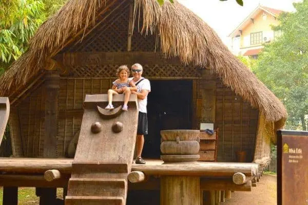 kids love the traditional villages at the museum of ethnology in vietnam. a dad and daughter on the porch of a straw cottage.