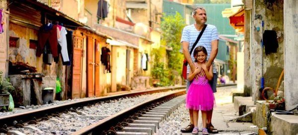 this railway village is a unique place in hanoi. a dad and daughter stand between the tracks a nd houses.