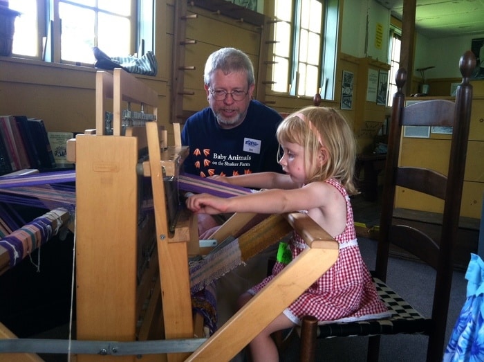 A young girl weaving on a loom at hancock shaker village