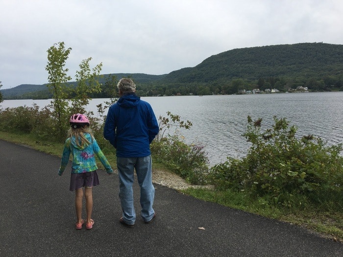 A dad and daughter pausing along a rail trail to admire the berkshire mountains and a lake