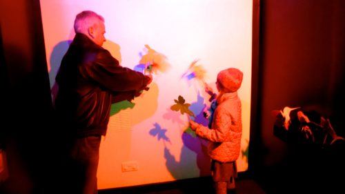 A dad and daughter play with light and shadows at a science museum