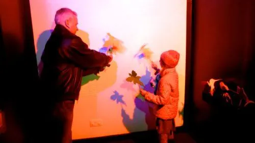 a dad and daughter play with light and shadows at a science museum