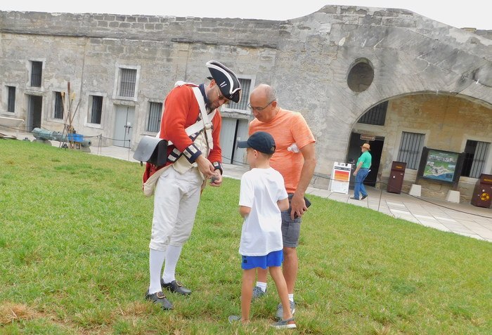 A volunteer shows a boy and dad the cochineal bugs that made red dye for colonial uniforms.