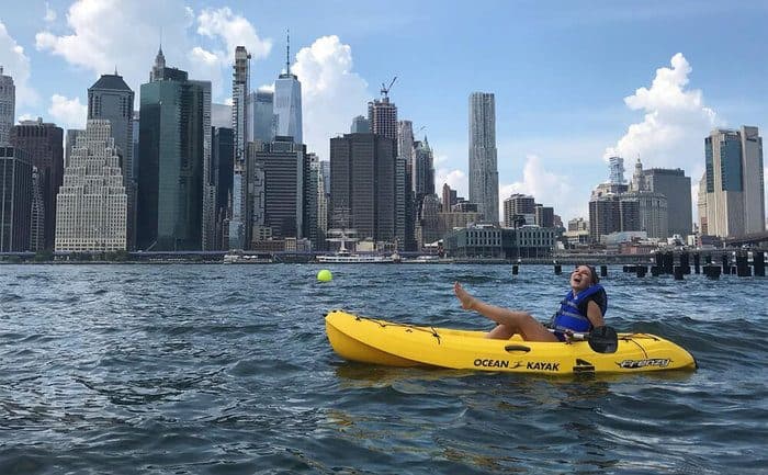 A girl has fun kayaking in the east river with manhattan behind her.