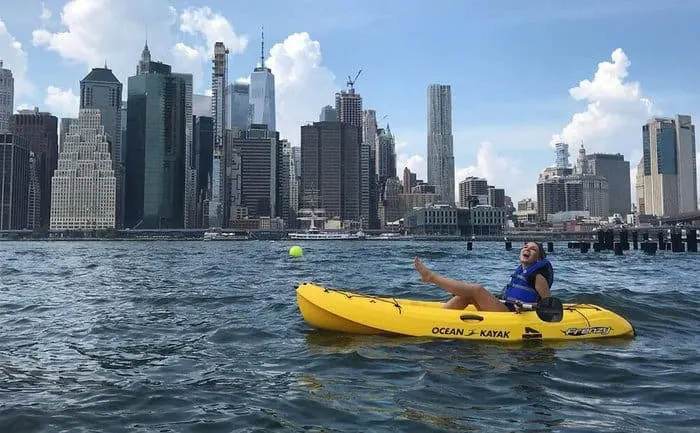 a girl has fun kayaking in the east river with manhattan behind her.