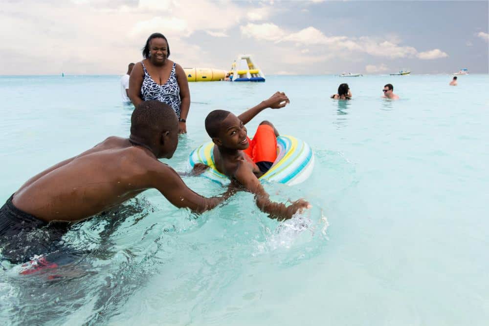 a family plays in the clear blue water at the alexandra resort in turks and caicos. a dad tipping his son out of a rubber tube.