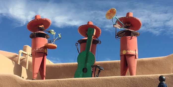 3 colorful mariachi statues on an adobe roof top in old town albuquerque.
