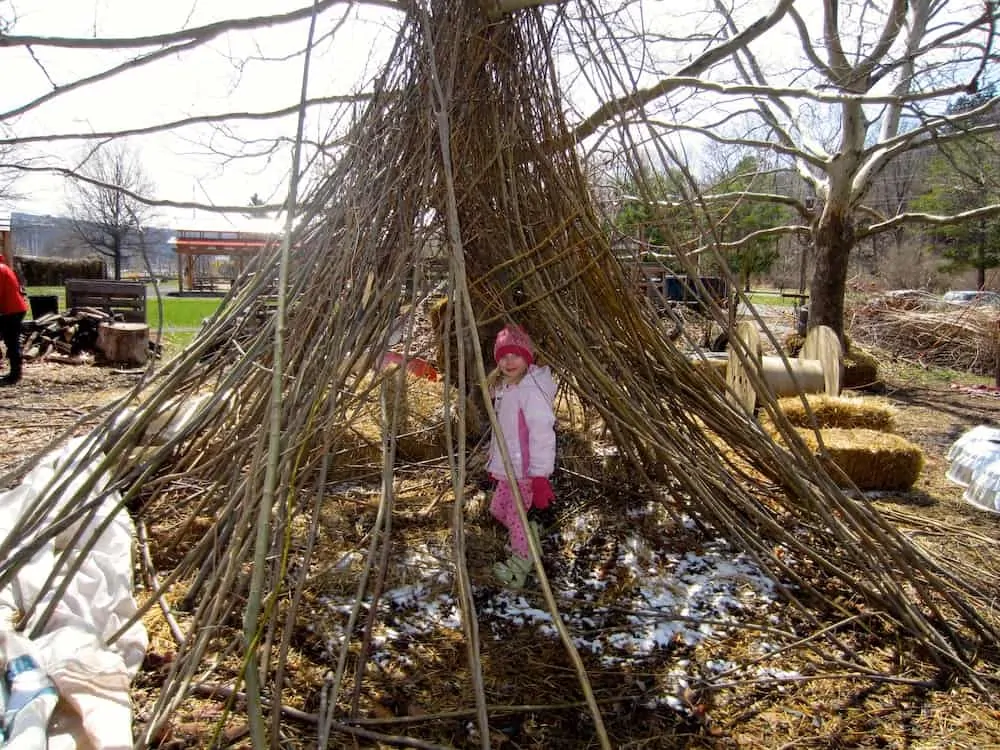 a girl plays in a teepee made of sticks at the ithaca childrens garden