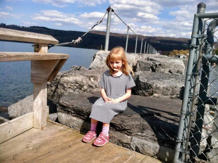 a girl sits by the lakefront outside of the watkins glen harbor hotel.