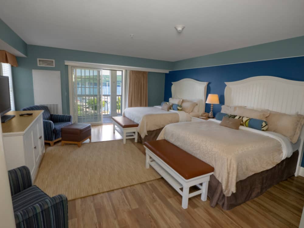 A room at the watkins glen harbor hotel with two bed and arm chairs, plus a blacony.