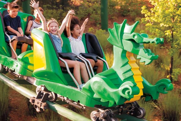 Kids ride a dragon roller coaster at legoland california on a fall day.