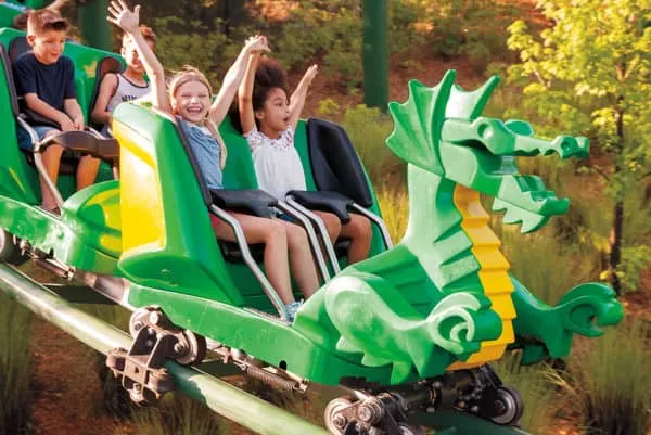 kids ride a dragon roller coaster at legoland california on a fall day. 