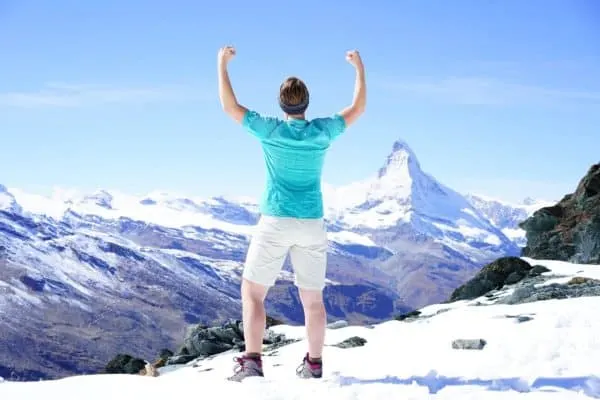 Here's How To Plan A Memorable Vacation With Your Teen a person exulting in their hiking victory in sight of the matterhorn.