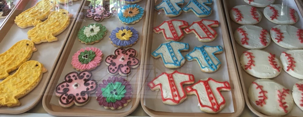 sugar cookies look like yellow chicks, spring flowers, baseballs and baseball jerseys in the window at schneider's bakery in cooperstown.