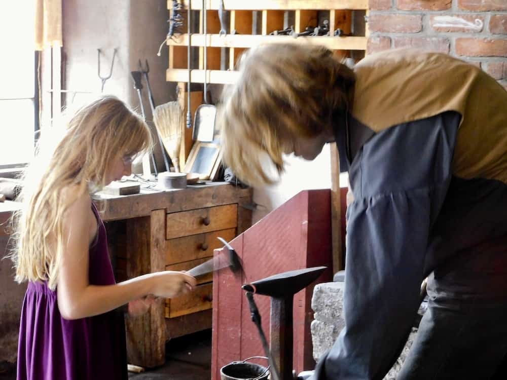 A blacksmith and a girl work on an iron project at the farmers' museum