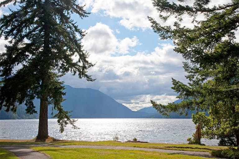 Lawn, pine trees, lake, mountains and sky. The view of crescent lake lodge in washington.