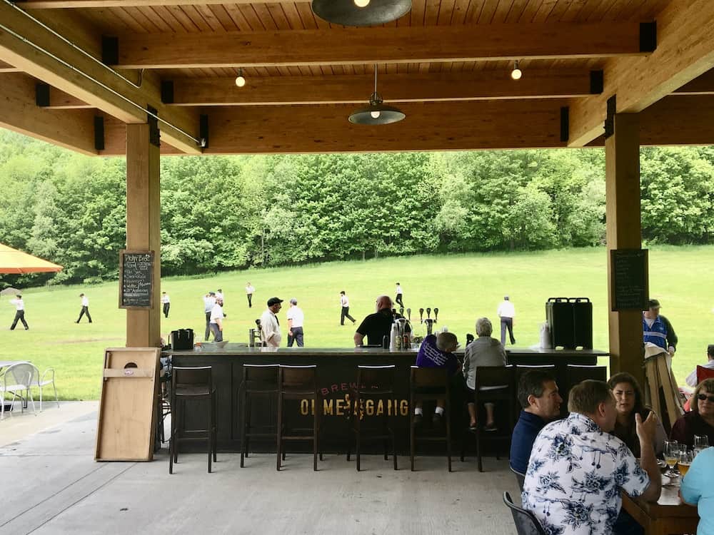 the outside bar and field behind ommegang brewery and tap house, a basebal game is happening.