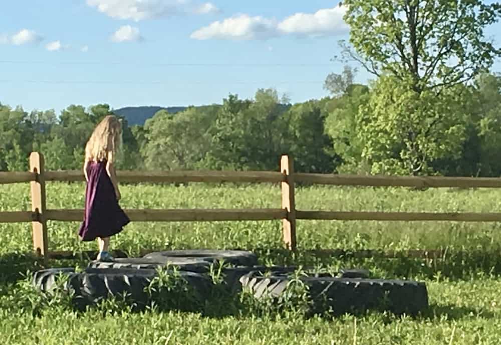 A girl hopping on tires in front of a split-rail fence in the yard of the kid-friendly red shed brewery.