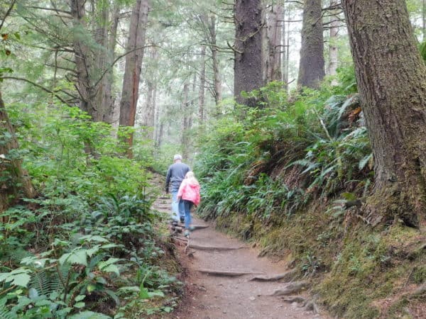 a dad and daughter head down the woodsy trail that leads to second beach on the olympic peninsula.