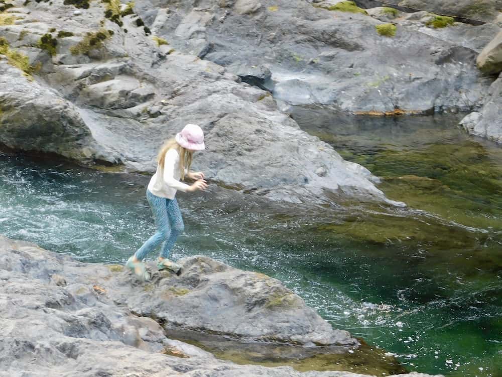 a tween enjoys jumping from rock to rock in the clear, rapid sol doc river.