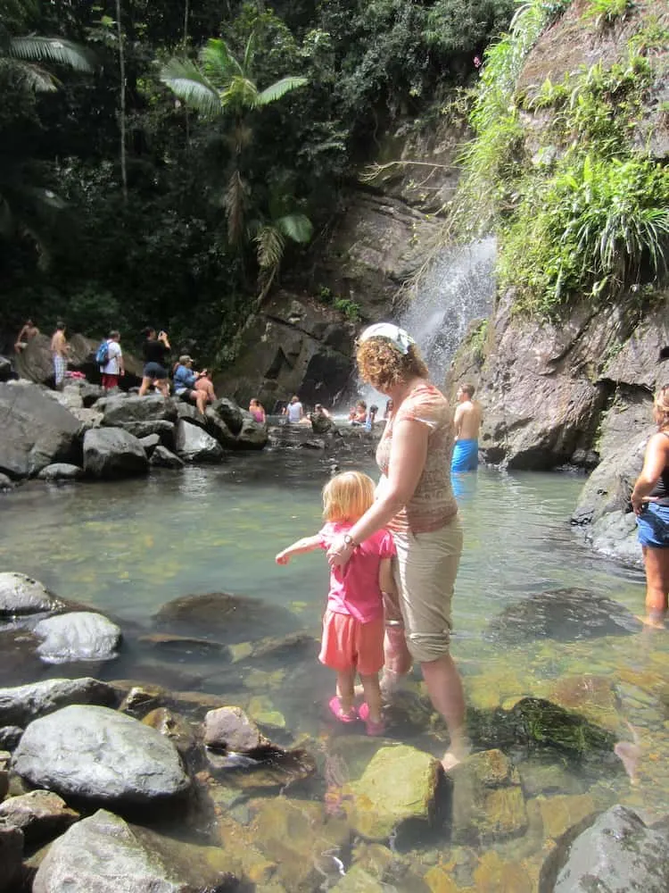 a mom and daughter explore the pools beneath a waterfall in puerto rico's el yunque national forest.