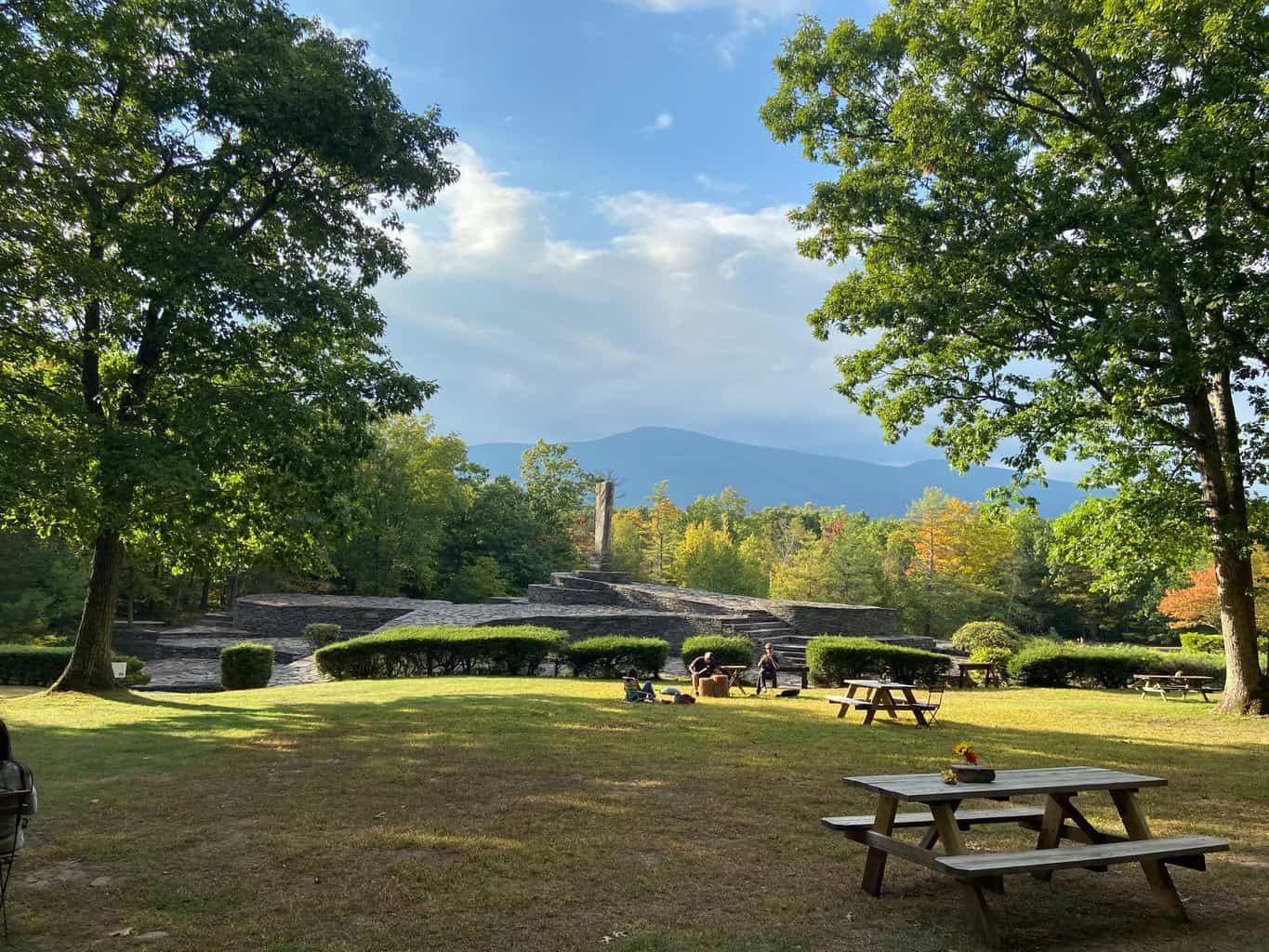 The stone structures of opus 40 with a picnnc table in the foreground and the catskill mountains behind. The foliage is changing color for fall
